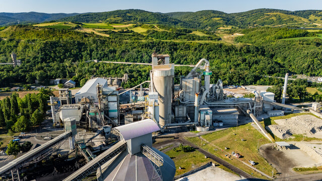Aerial view of the Holcim Serbia cement factory in Beocin, featuring industrial structures, silos, and conveyor belts set against green hills Beocin, Vojvodina, Serbia.