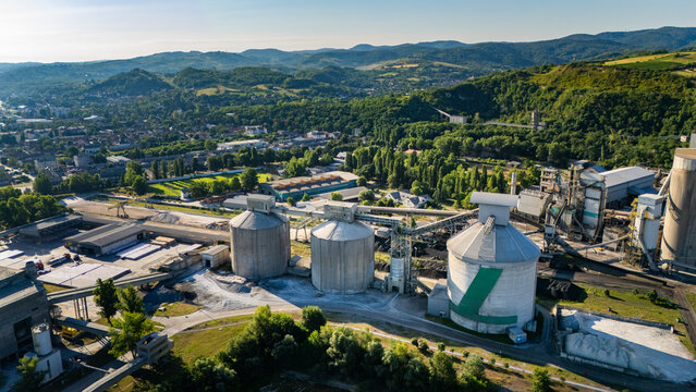 Aerial view of the Holcim cement factory with large industrial silos and processing facilities set against a green landscape in Beocin, Vojvodina, Serbia.
