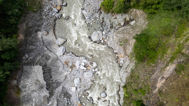 Aerial view of the Langtang River flowing through a rugged landscape with large boulders, rocky banks, and lush green trees in Langtang National Park, Bagmati Province, Nepal.