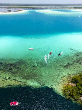 Aerial view of Cenote Negro with vibrant turquoise waters contrasting with deep blue depths, surrounded by lush vegetation and boats, Bacalar, Quintana Roo, Mexico.