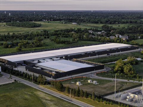 Aerial view of data center with large flat roof and modern dark facade surrounded by green fields and trees in Hoffman Estates, Illinois, United States.
