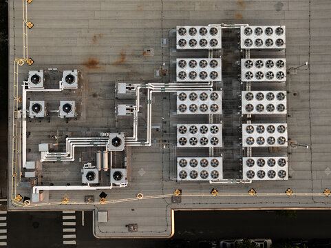 Aerial view of a data center roof featuring rows of industrial cooling fans, complex piping systems, and ventilation units in Cambridge, Massachusetts, United States.