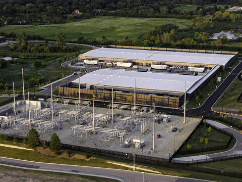 Aerial view of the data center facility with industrial buildings and an electrical substation surrounded by green landscape and roads in Hoffman Estates, Illinois, United States.