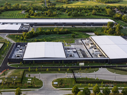 Aerial view of a modern data center facility with large white rooftops, industrial cooling units, and surrounding green landscape during the golden hour in Hoffman Estates, Illinois, United States.