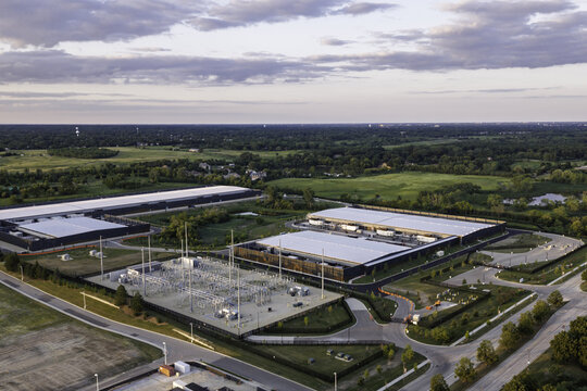 Aerial view of a large data center complex featuring multiple industrial buildings, a power substation, and surrounding green fields in Hoffman Estates, Illinois, United States.