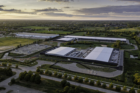 Aerial view of a modern data center complex with large industrial buildings, a power substation, and surrounding green space in Hoffman Estates, Illinois, United States.