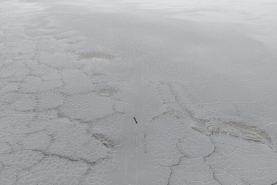 Aerial view of the Uyuni Salt Flat with its vast hexagonal salt crust patterns and a lone person walking across the white landscape in Potosi Department, Bolivia.