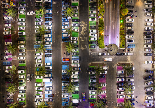 Aerial view of a car lot at a mall with rows of parked vehicles, palm trees, and marked parking spaces in Hod Hasharon, Center District, Israel.