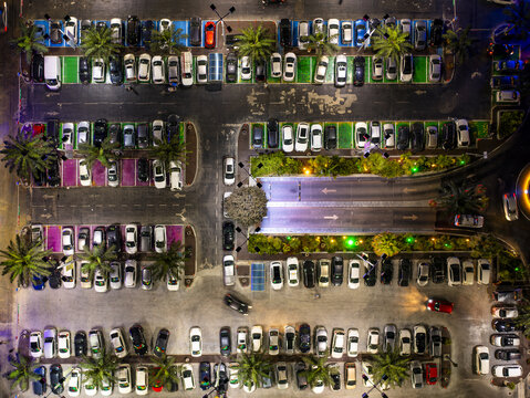 Aerial view of a car lot at a mall with rows of parked vehicles, palm trees, and illuminated asphalt lanes in Hod Hasharon, Center District, Israel.