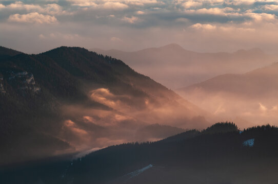 Aerial view of Dumbier in the Low Tatras mountains with rolling peaks, dense pine forests, and golden hour light filtering through clouds in Liptovsky Jan, Zilina Region, Slovakia.