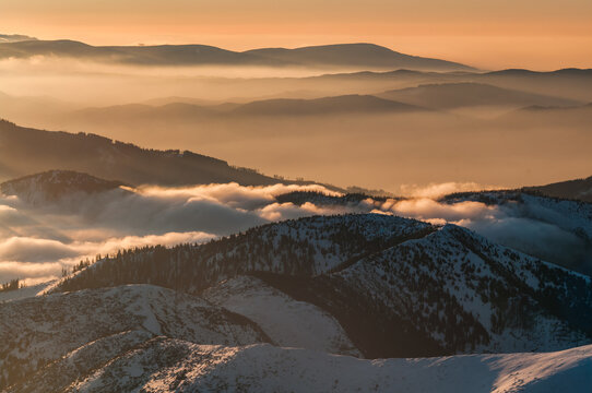 Aerial view of the Low Tatras mountains from Dumbier peak, featuring snow-covered slopes, evergreen forests, and clouds at golden hour in Liptovsky Jan, Zilina Region, Slovakia.
