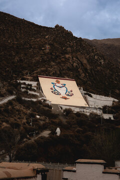 View of the large thangka display wall on the rocky hillside of Sera Monastery with traditional Tibetan architecture and mountain landscape in Lhasa, Tibet, China.