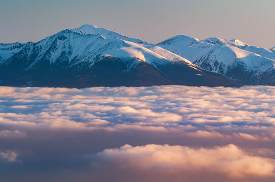 Aerial view of Western Tatras mountains rising above a sea of clouds during sunrise with snow-capped peaks and soft golden light in Jamnik, Zilina Region, Slovakia.