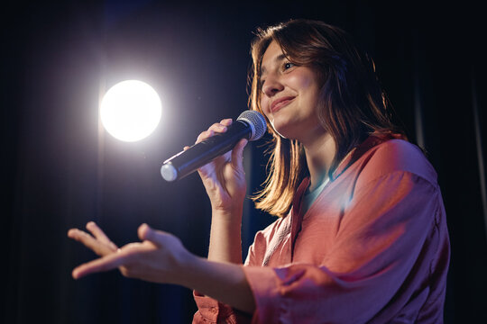 Caucasian girl holding microphone and performing on stage during student theater rehearsal. Image suitable for promoting youth arts programs and drama education, low angle view