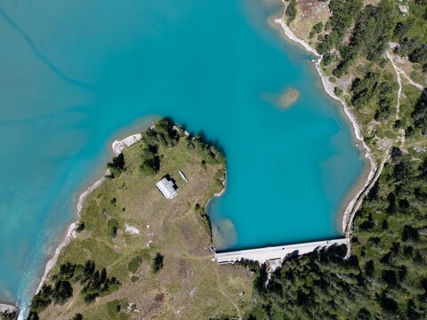 Aerial view of the turquoise waters of Lago di Palu and the Palu Hydroelectric Power Plant dam surrounded by alpine forests in Poschiavo, Grisons, Switzerland.