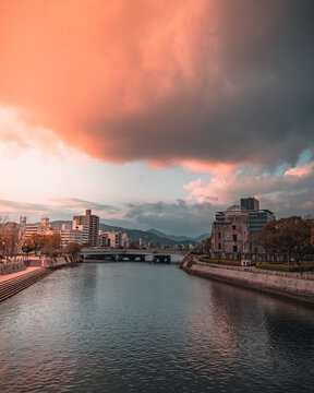 View of the Atomic Bomb Dome along the Motoyasu River in Hiroshima under a dramatic sunset sky with orange clouds, Japan.