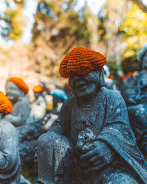 View of stone Jizo statues wearing bright orange knitted hats in a serene outdoor setting in Japan.