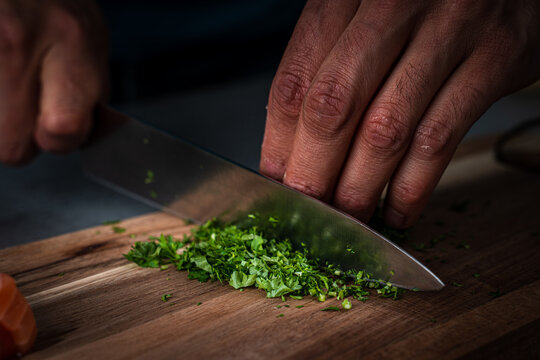 View of a chef chopping fresh green herbs on a wooden cutting board with a piece of raw salmon nearby in Tromso, Troms, Norway.
