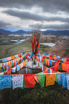 View of colorful prayer flags at Shangri-La City with a panoramic view of the valley and mountains under a cloudy sky in Diqing Tibetan Autonomous Prefecture, Yunnan, China.