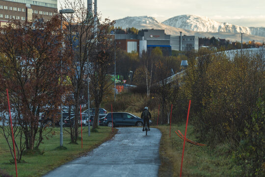 Tromso, Troms, Norway - 24 July 2026: View of a cyclist riding along a paved path with cars and snow-capped mountains in the background.