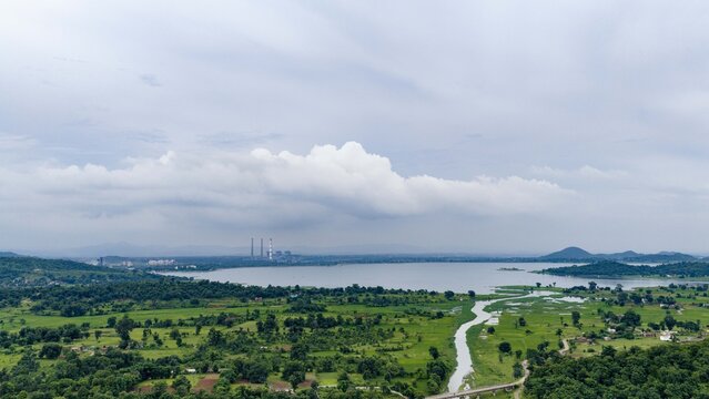 Aerial view of Patratu Dam surrounded by lush green fields, rolling hills, and a power plant in the distance under a cloudy sky Labga, Jharkhand, India.