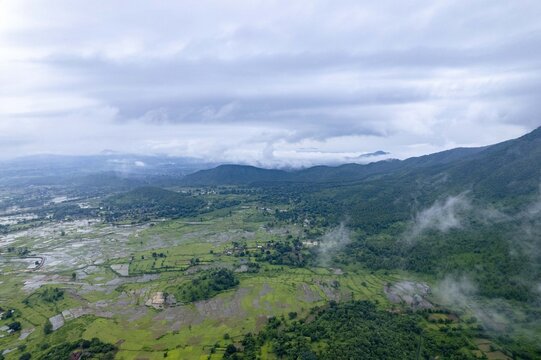 Aerial view of lush green terraced fields and rolling hills under a cloudy monsoon sky in Jharkhand, India.