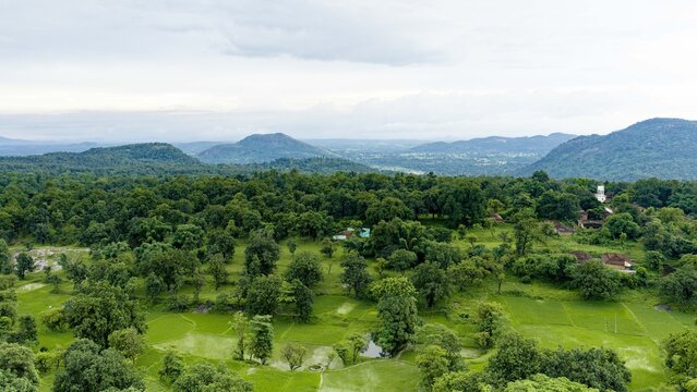 Aerial view of a lush green village landscape surrounded by dense forests and rolling hills during the monsoon season in Jharkhand, India.