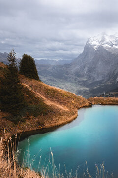 View of Kleine Scheidegg with a turquoise alpine lake, grassy slopes, and snow-capped mountains in the background in Lauterbrunnen, Canton of Bern, Switzerland.