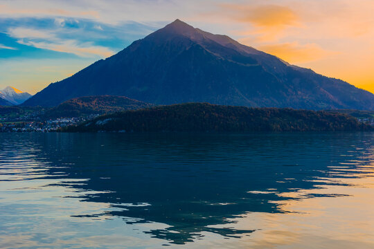 View of Mount Niesen reflected in the calm waters of Lake Thun during golden hour in Reichenbach im Kandertal, Canton of Bern, Switzerland.