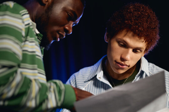 African American young adult man and teenager reading script together during student theater rehearsal, perfect for youth arts education and drama school marketing, close up