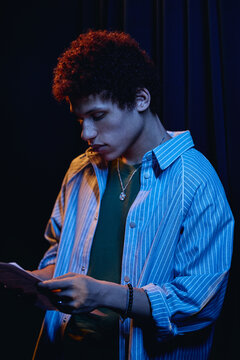 Young male teenager reading script backstage during student theater rehearsal, preparing for performance. Image useful for drama school promotions, vertical