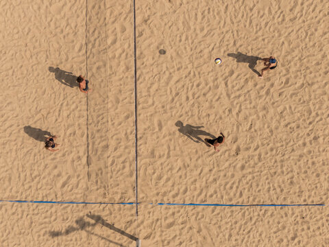 Aerial view of beach volleyball players and ball in play on sand court divided by net, outdoor summer sport action concept.