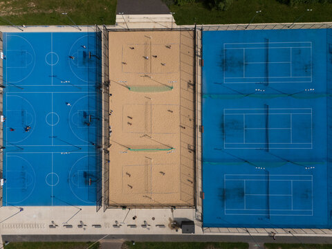 Aerial top-down view of outdoor sports complex with basketball, beach volleyball and tennis courts, urban multi-sport facility and recreation concept.