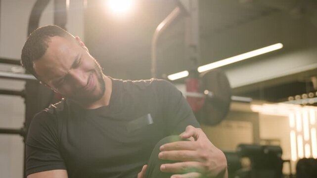 African American male man bodybuilder massaging painful knee in gym after workout injured athlete stretching leg muscle pain sprain cramp suffering fitness trauma strength exercise recovery indoors