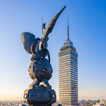 Aerial view of Torre Latinoamericana rising above the city skyline, framed by a bronze eagle sculpture in the foreground under a clear blue sky. Ciudad de Mexico, Ciudad de Mexico, Mexico.