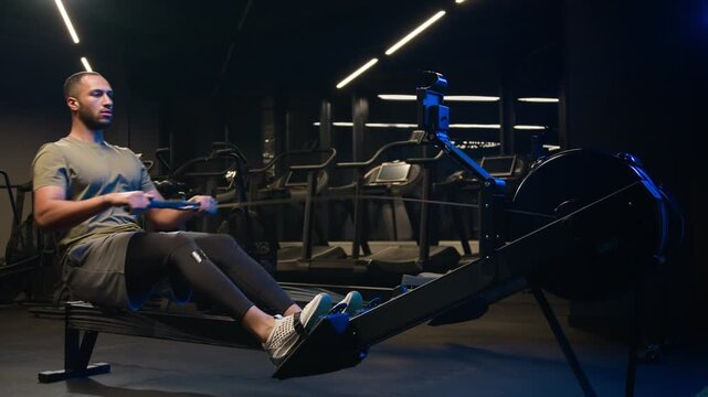 African American male man bodybuilder using rowing machine in gym sportsman hard strength workout athlete pulling low row exercise effort motivation fitness trainer building muscles endurance indoors