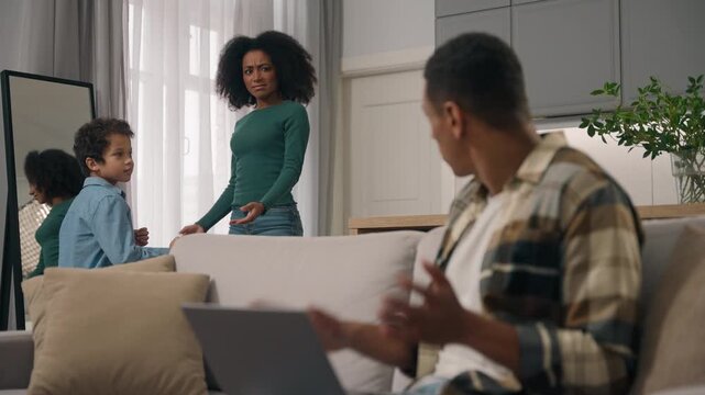 Angry African American father yelling complaining while mother and little boy child dancing having fun distracting dad working laptop notebook technology indoors home family mom kid conflict indoor