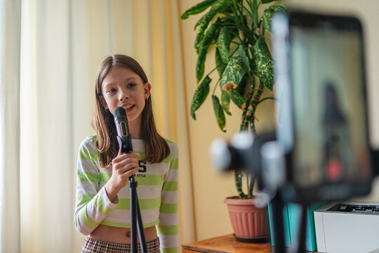 Young content creator recording music video on smartphone with microphone at home