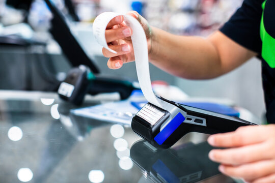 Selective focust to Cashier tearing off a paper receipt from a credit card payment terminal at a store counter. Close-up of modern POS transaction and retail shopping checkout process.