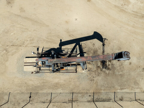 Aerial view of an oil pump jack casting a long shadow on the sandy ground in an oil field in Bakersfield, California, United States.