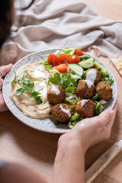 Person holding plate of falafel with hummus and fresh salad. Close up
