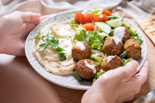 Person holding plate of falafel with hummus and fresh salad. Close up