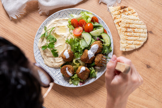 Person holding plate of falafel with hummus and fresh salad. Close up