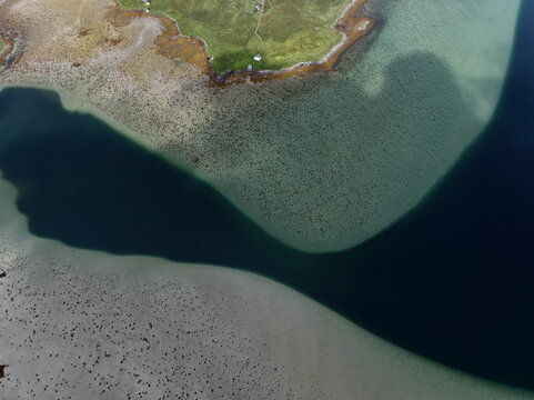Aerial view of the coastal landscape near Lofoten Beach Camp with clear turquoise water, sandy shoals, and green grassy terrain in Ramberg, Nordland, Norway.