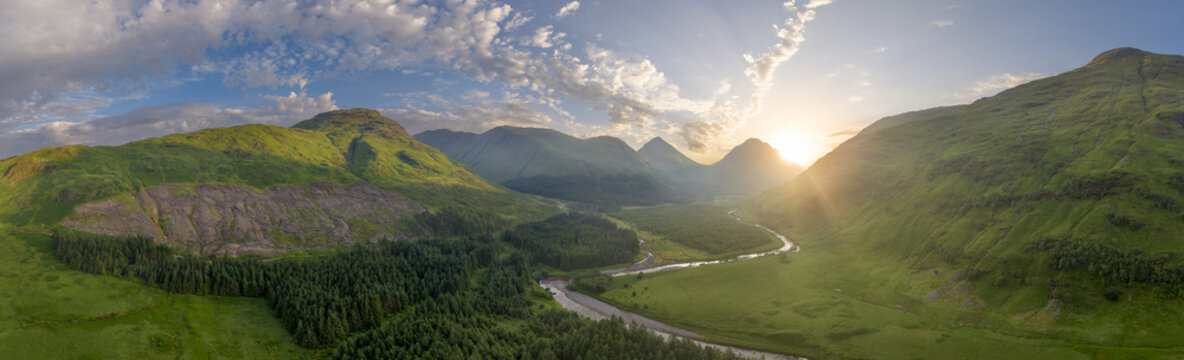 Aerial view of the Glen Etive featuring lush green mountains, a winding river flowing through the glen, and a vibrant sunset casting a golden glow over the landscape in Scotland.