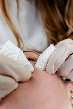 Professional beautician wearing face shield and gloves performs a deep cleansing facial treatment on a client in a spa clinic, focusing on skincare and hygiene.