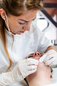 Professional beautician wearing face shield and gloves performs a deep cleansing facial treatment on a client in a spa clinic, focusing on skincare and hygiene.