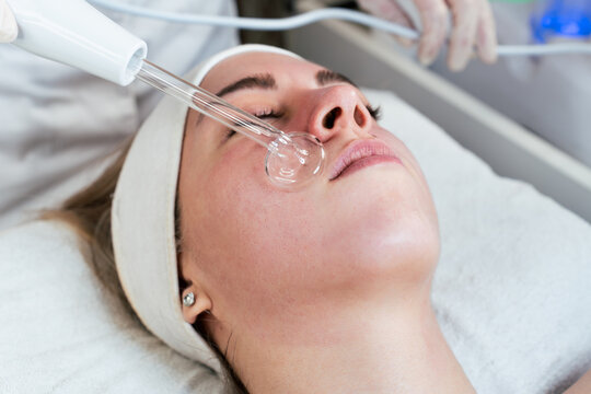 Cosmetologist using frequency darsonval device for skin rejuvenation, acne treatment, and anti-aging therapy in a modern medical spa.