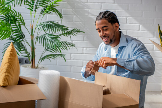 Young african american man packing cardboard boxes with bubble wrap during a move into a modern, bright apartment