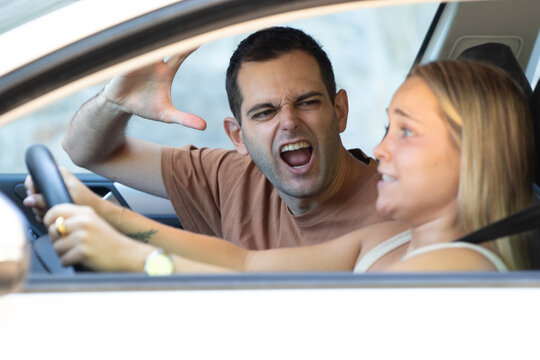 A young couple arguing heatedly inside a car; the man is shouting with his hand raised while the woman appears surprised and upset. An example of tense couple conflict and road rage